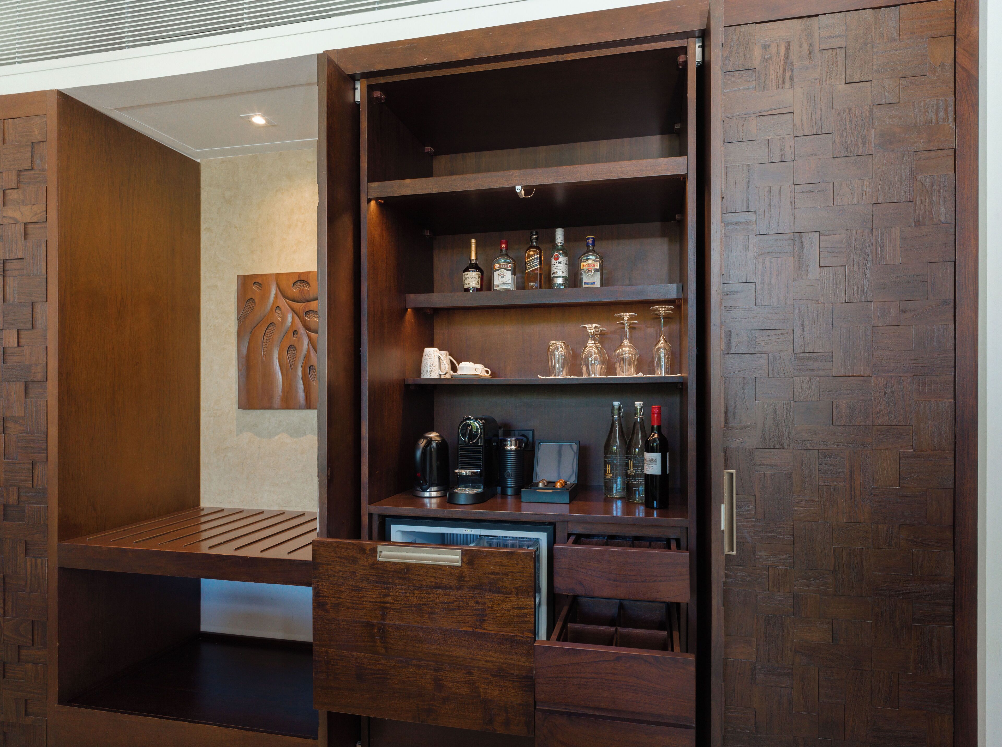 A wooden cabinet with shelves holding bottles, glasses, and a coffee maker.