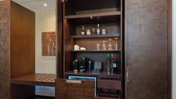 A wooden cabinet with shelves holding bottles, glasses, and a coffee maker.