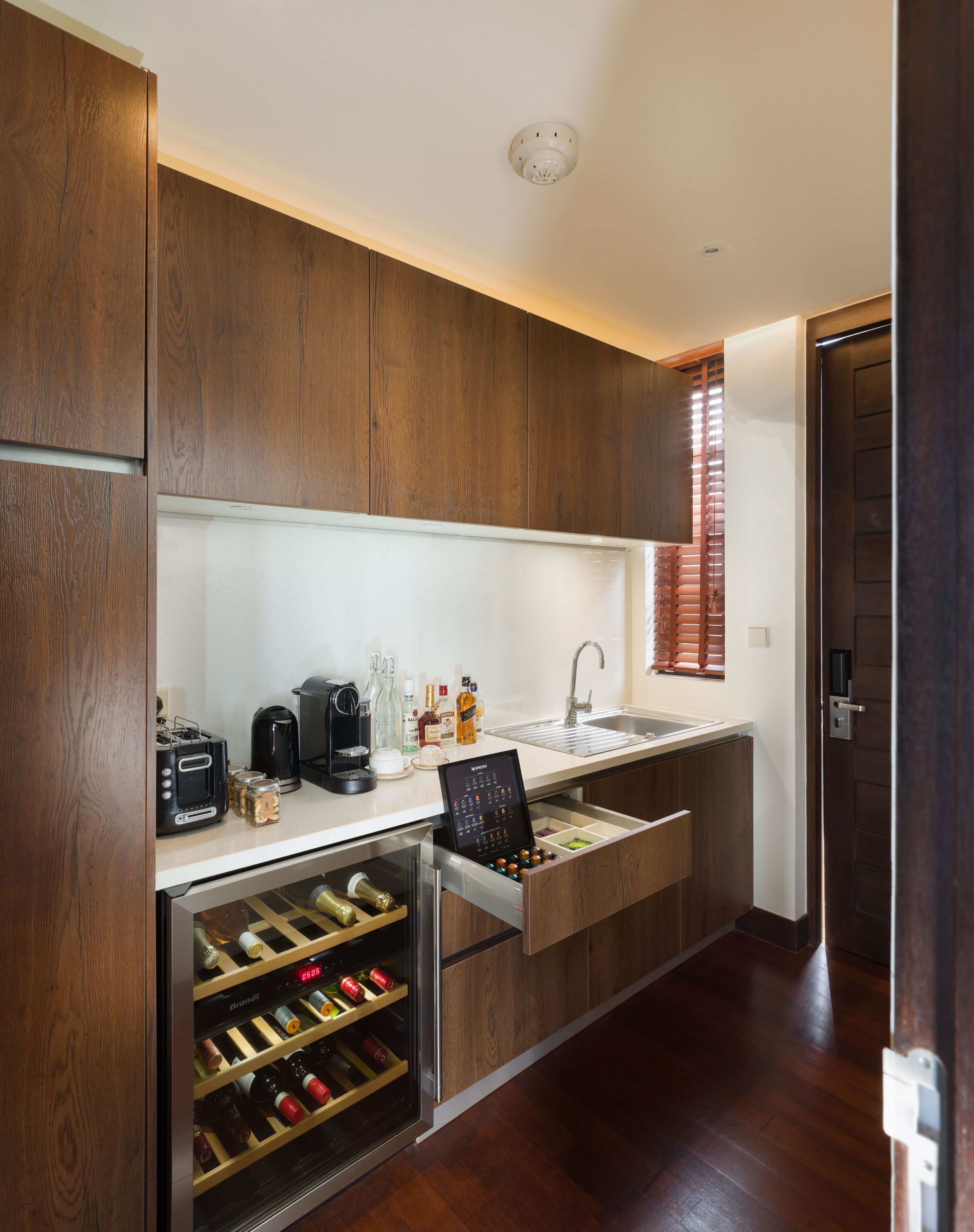 A modern kitchen with wooden cabinets, a wine cooler, and a built-in coffee maker.