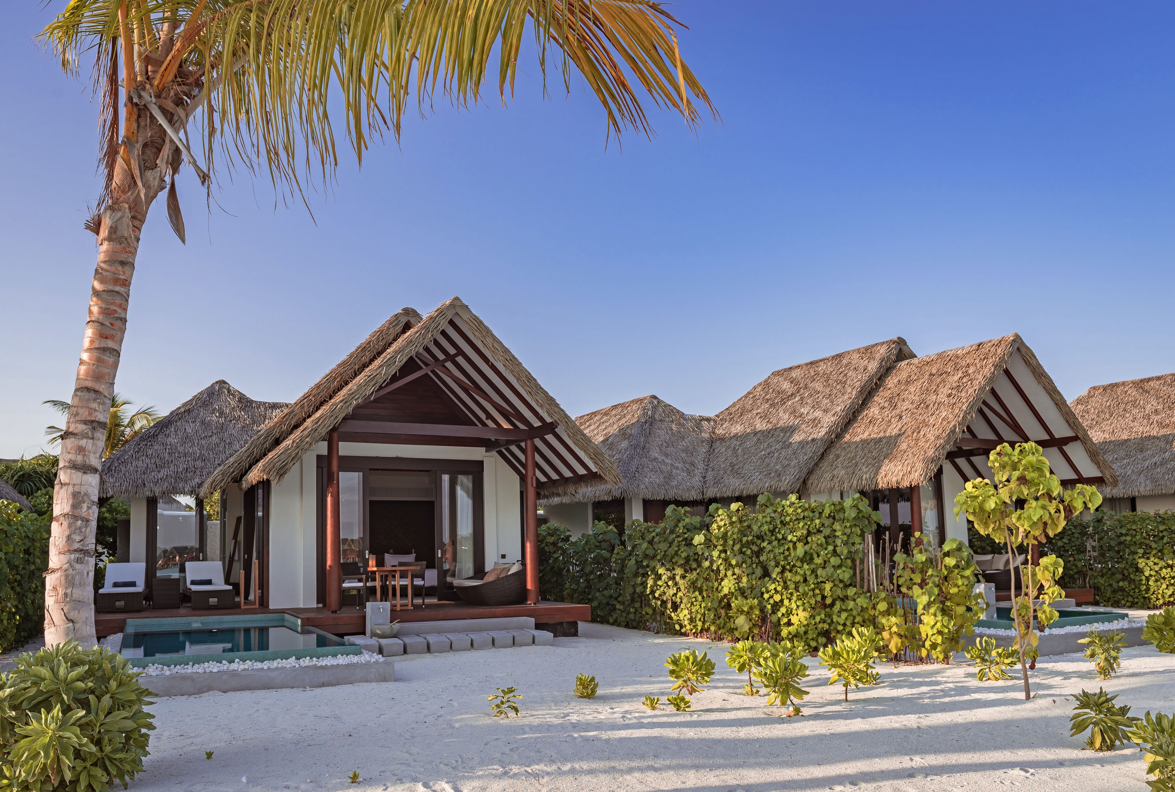 Een resort met villa's met rieten daken, een zwembad en tropische beplanting.