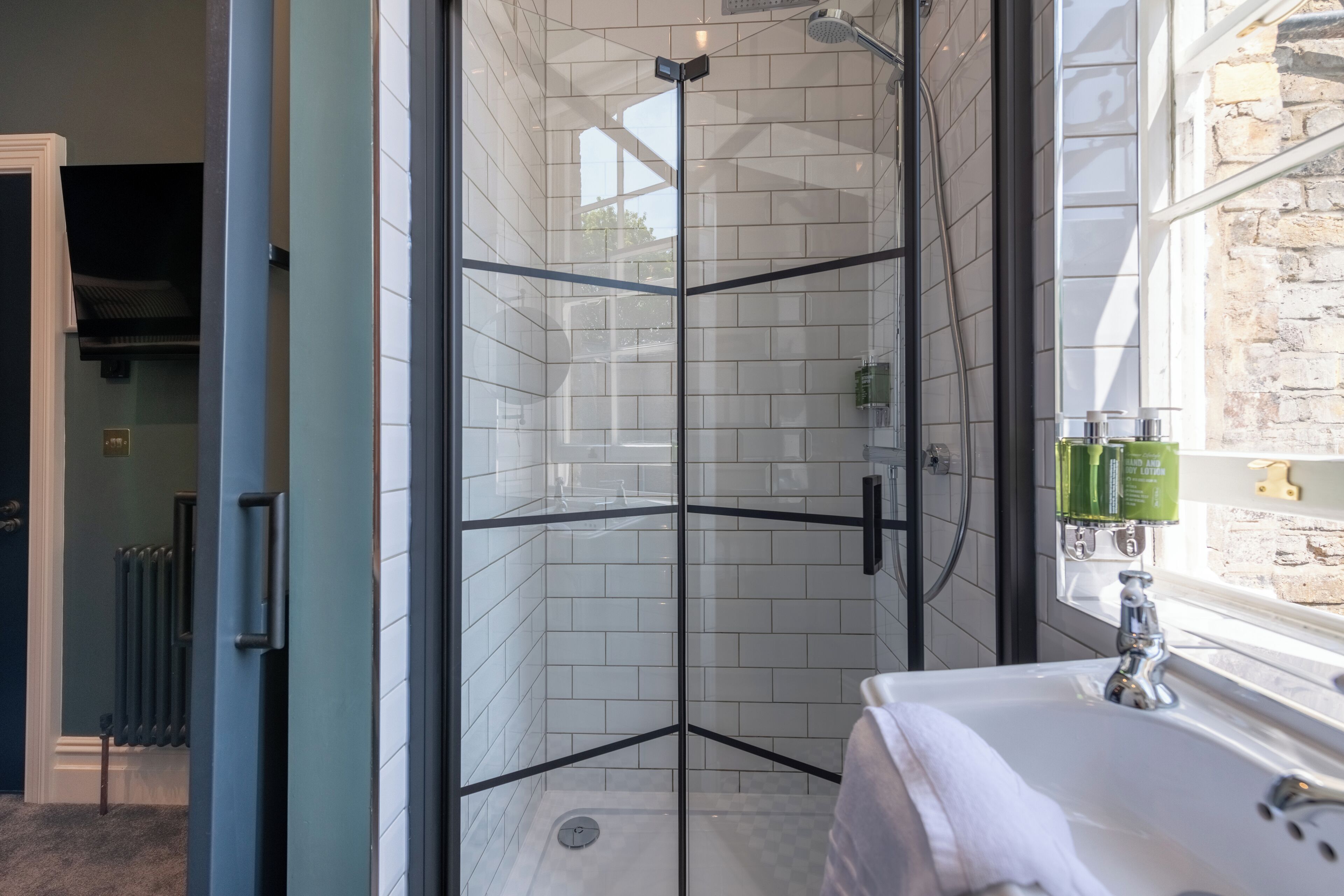 A modern bathroom with a glass-enclosed shower, a white sink, and a window with a view of the outside.