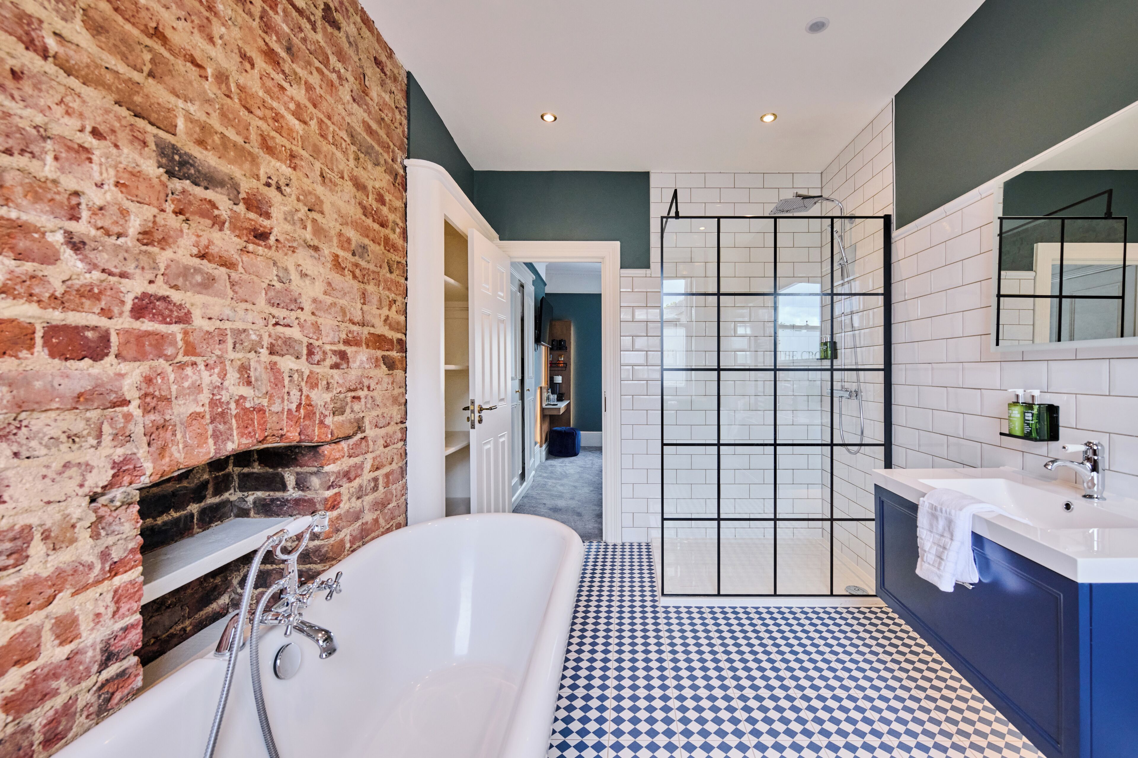 Ein modernes Badezimmer mit Backsteinwand, freistehender Badewanne, begehbarer Dusche und blau-weiß kariertem Boden.