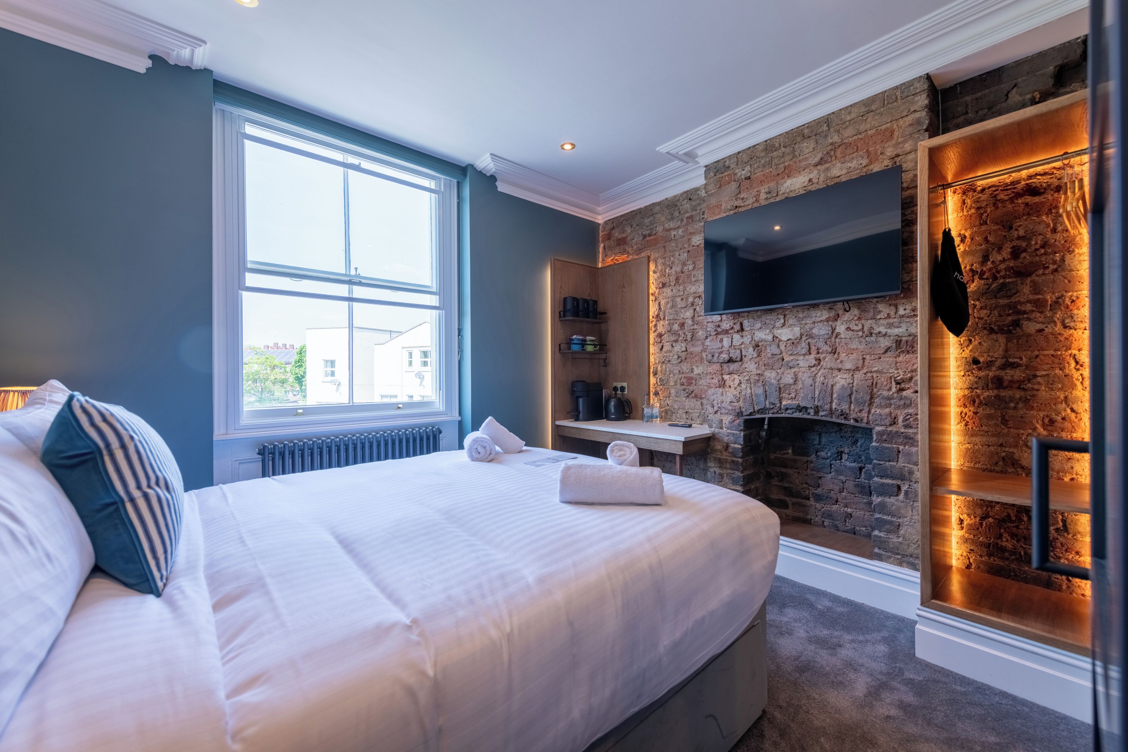 Habitación de hotel con una cama grande, una chimenea de piedra, un televisor en la pared y un ventanal con vistas al exterior.