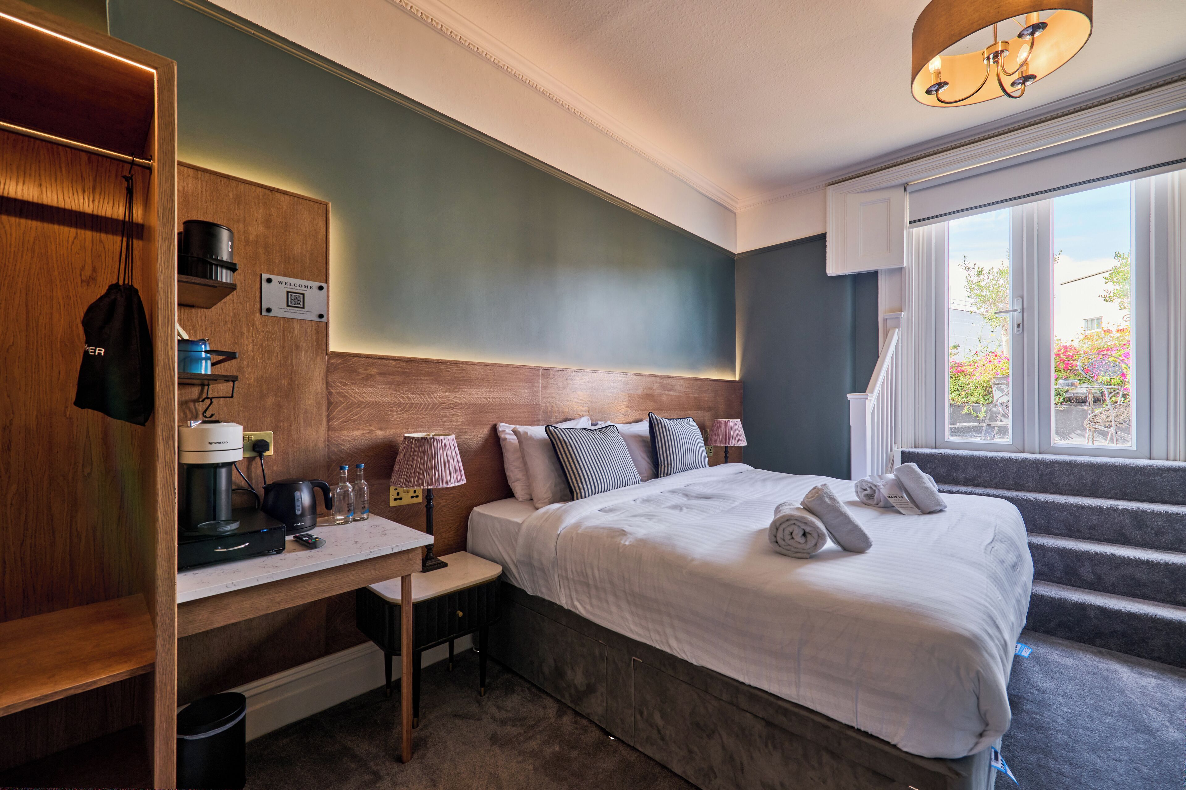 A hotel room with a bed, bedside table, and a view of the outdoors.