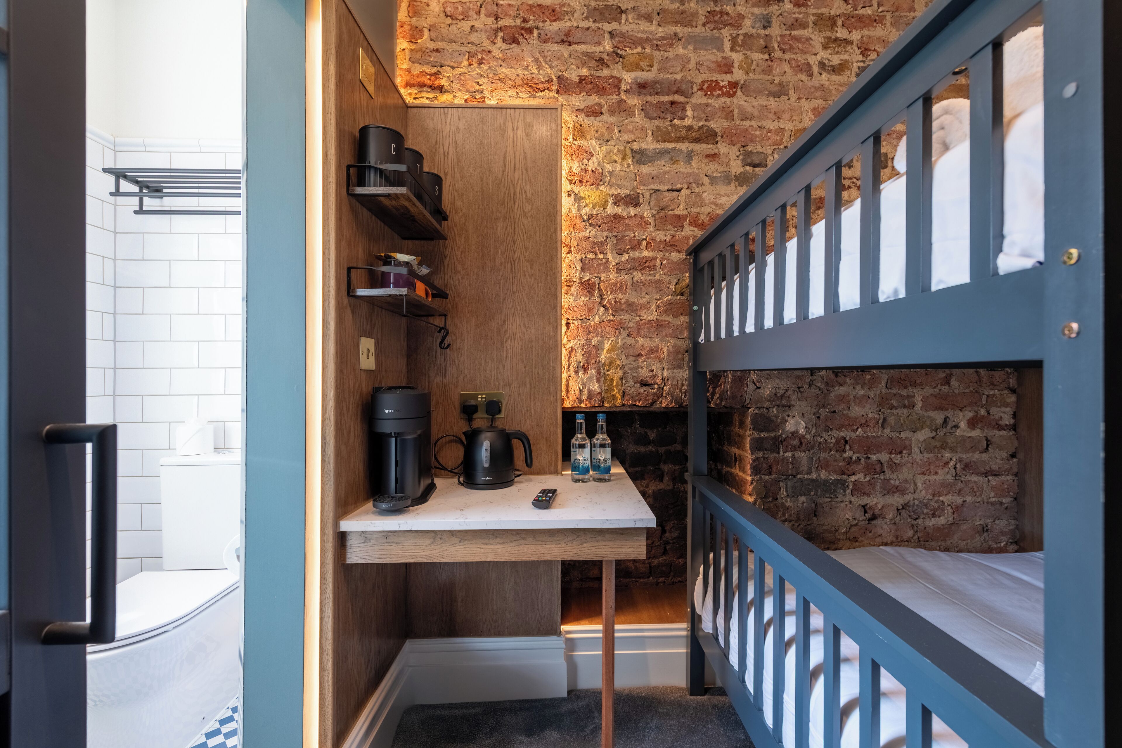 A compact room with a bunk bed, a small table with coffee-making equipment, and a brick wall.