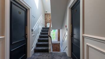 A hallway with black doors numbered 15 and 12, carpeted stairs, and a brick wall.