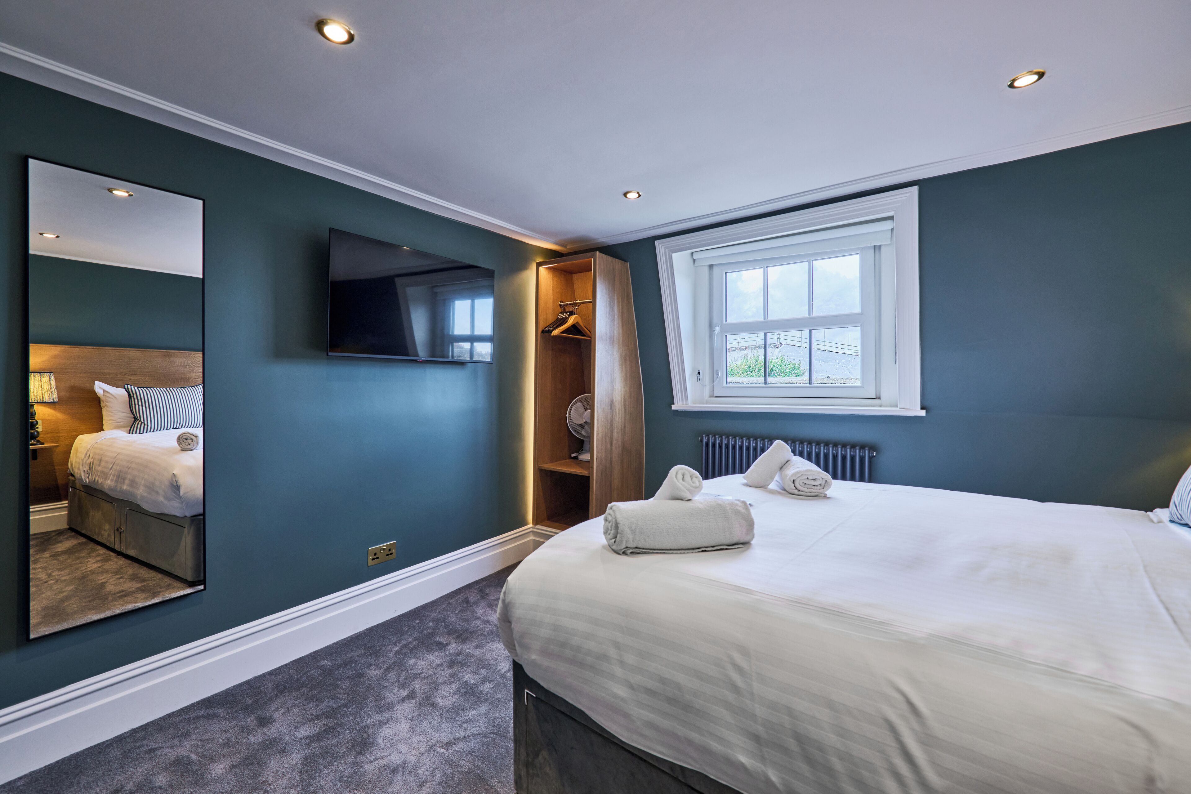 A bedroom with a large bed, a walk-in closet, a television, and a window with a view.