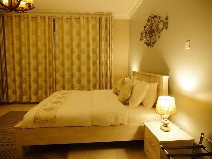 A bedroom with a bed, a nightstand, a lamp, a wall decoration, and curtains.