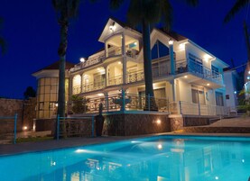 A multi-story house with a swimming pool in front.