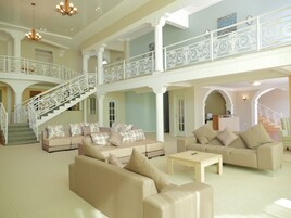 A spacious living area with a high ceiling, a staircase with ornate railings, and multiple seating areas with sofas and a coffee table.