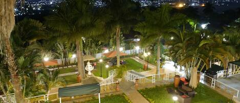 A well-lit outdoor area with a fountain, palm trees, and a view of a cityscape at night.