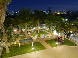 A well-lit outdoor area with a fountain, palm trees, and a view of a cityscape at night.