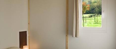 A bedroom with a bed, a window with a curtain, and a view of greenery outside.