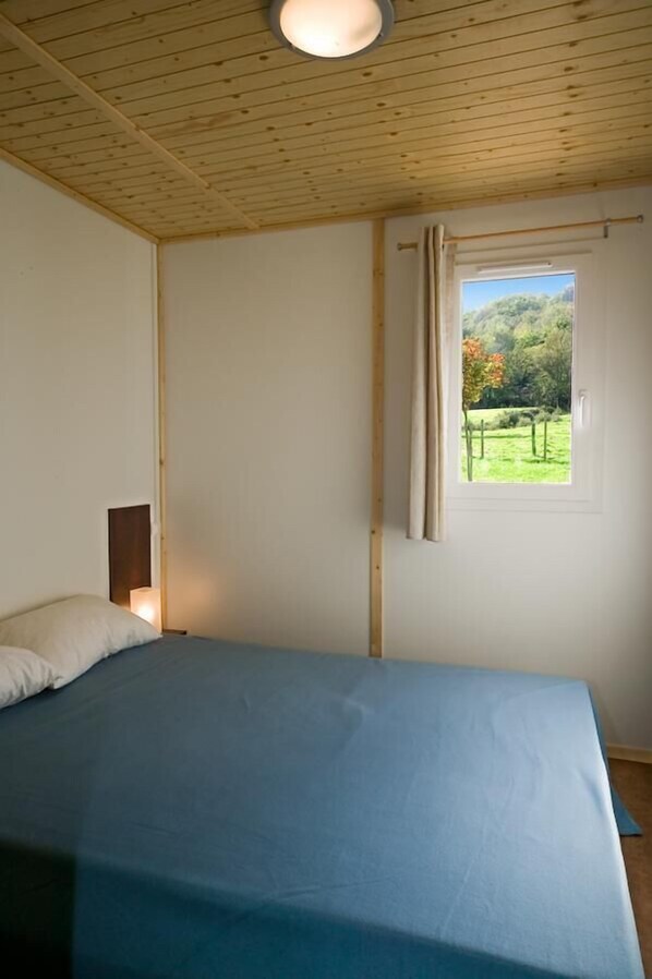 Une chambre à coucher avec un lit, une fenêtre avec un rideau et une vue sur la verdure à l’extérieur.