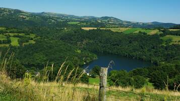 A panoramic view of a lush valley with a lake, surrounded by rolling hills and dense forests.