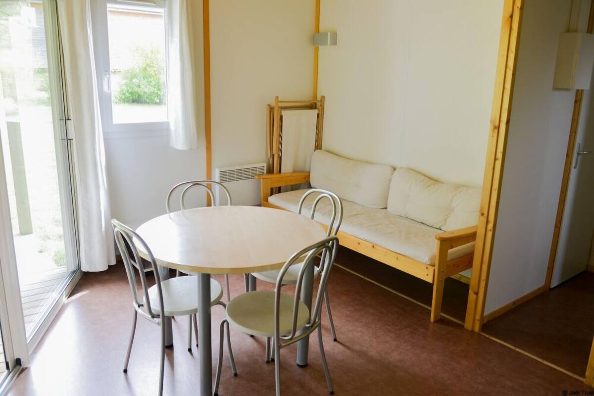 Um quarto com uma mesa redonda e quatro cadeiras, um banco de madeira e uma janela com cortinas.