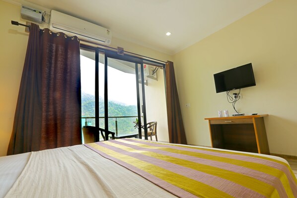 Ein Hotelzimmer mit Bett, Fernseher, Klimaanlage, Schreibtisch und Blick ins Freie.