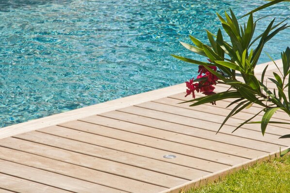 Ein Holzdeck an einem klaren, blauen Pool mit Pflanze und roten Blüten.