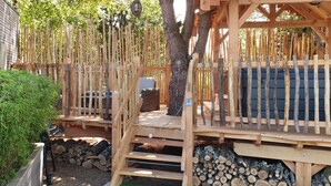 A wooden deck with a ladder leading to a covered seating area, surrounded by a fence and trees. - Chambre d'hôtes Le Clos des Romarins (Saint-Palais-sur-Mer)