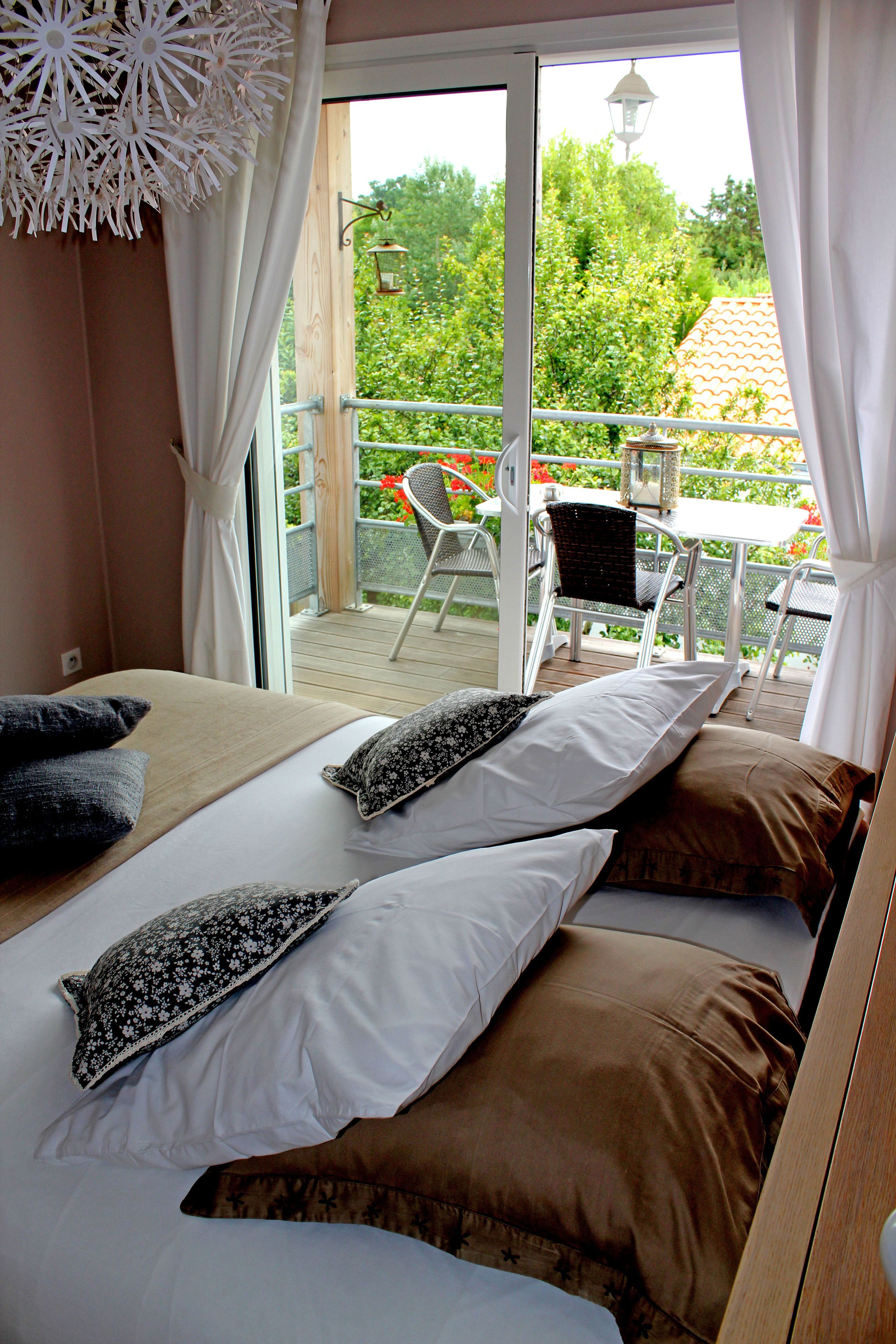 A bedroom with a bed, pillows, and a view of an outdoor balcony with chairs and a table.