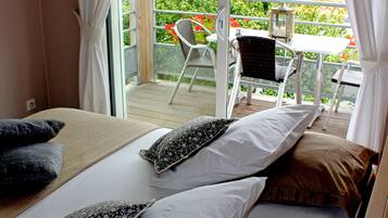 A bedroom with a bed, pillows, and a view of an outdoor balcony with chairs and a table.