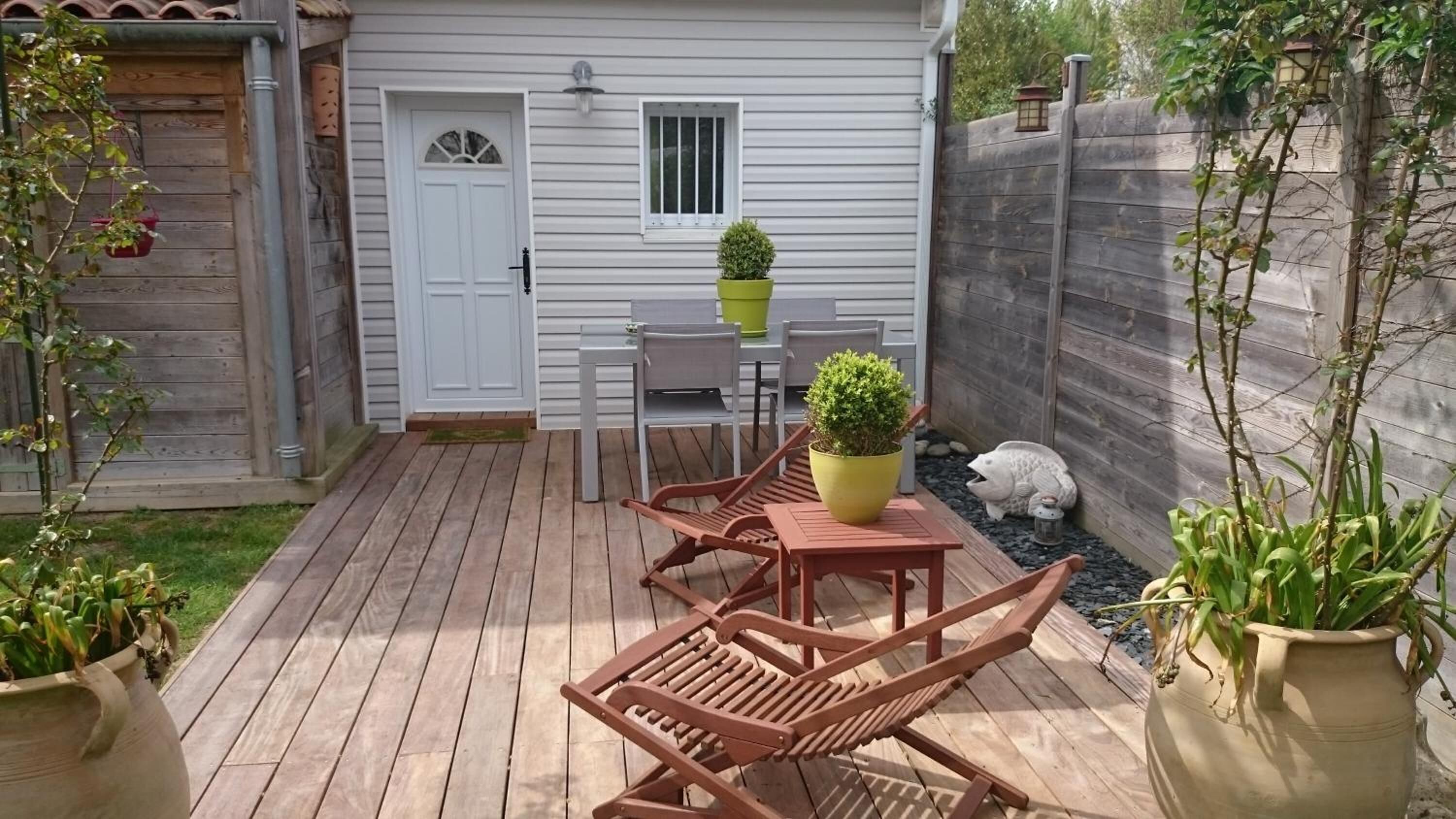 Une terrasse en bois avec une table et des chaises, une plante en pot et une petite statue.