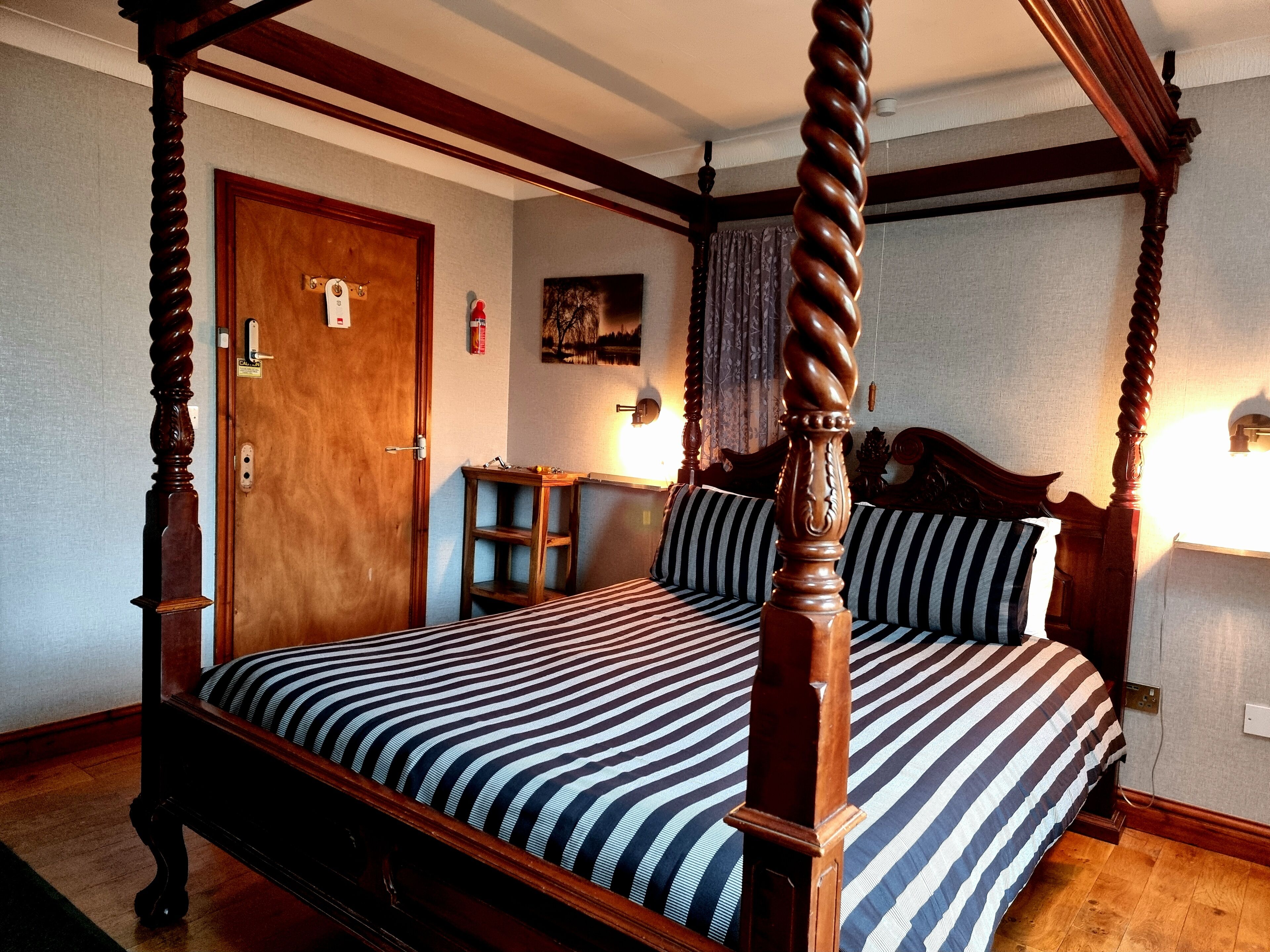 Un letto a baldacchino con copriletto a righe, un comodino in legno e un quadro appeso al muro.