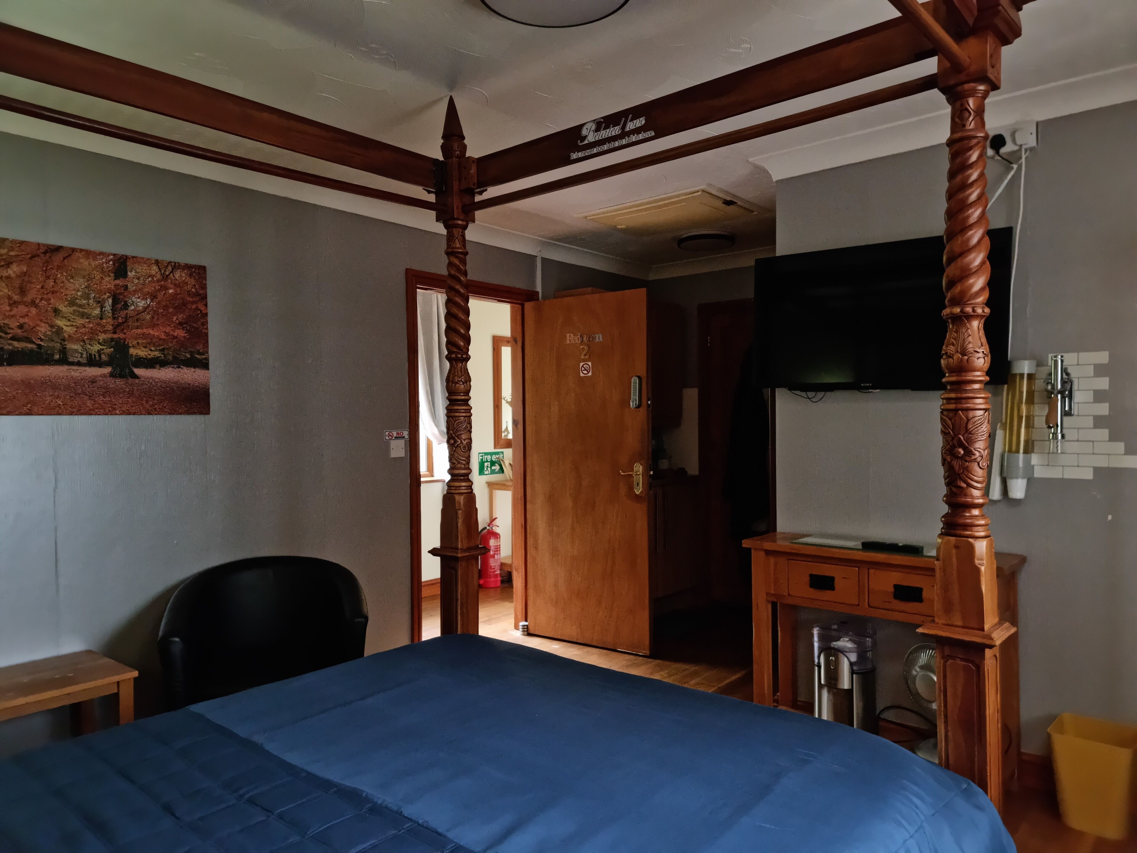 Una habitación con una cama con dosel, un escritorio de madera, una silla y un televisor instalado en la pared.