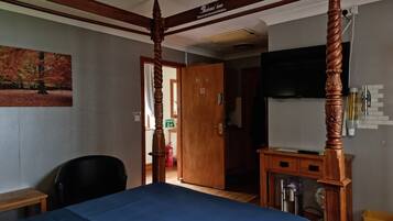Una habitación con una cama con dosel, un escritorio de madera, una silla y un televisor instalado en la pared.