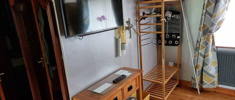 A room with a wooden desk, a TV mounted on the wall, a bunk bed with a shelf, and a radiator.