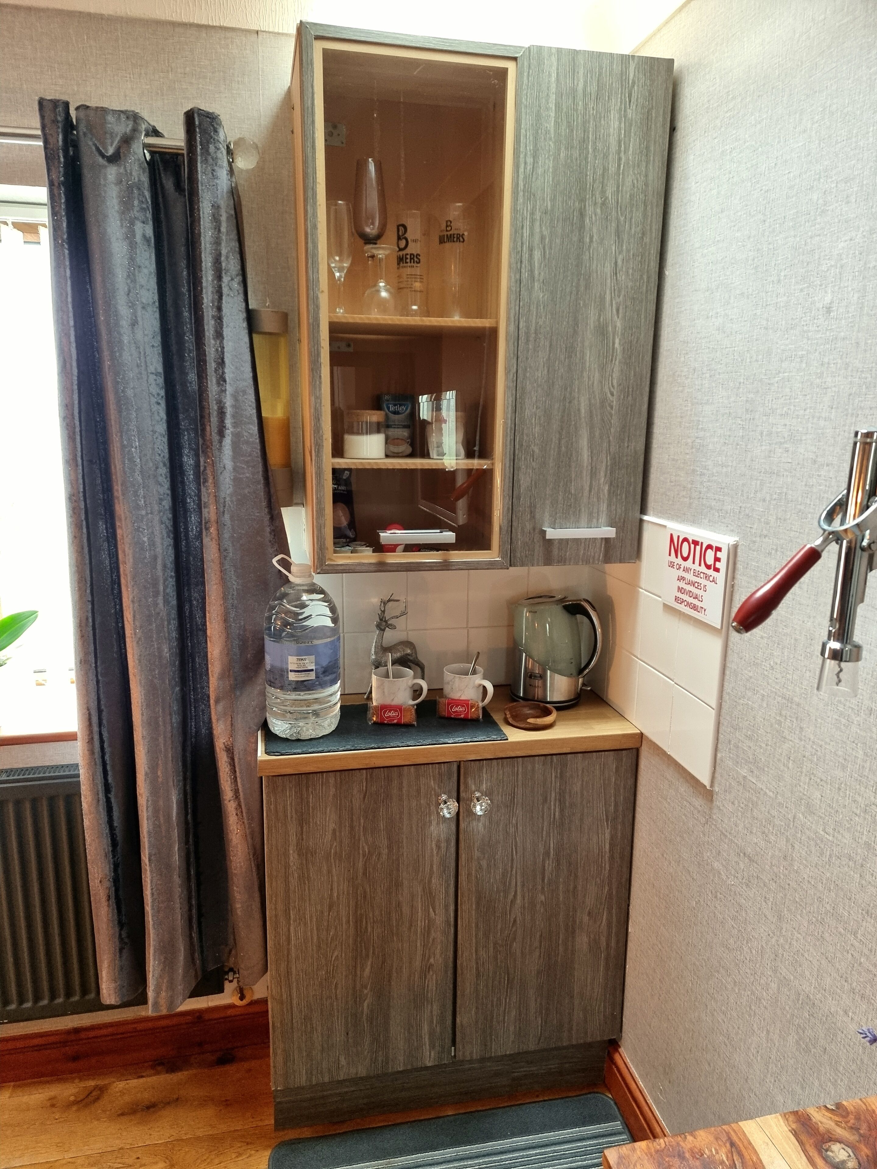 A compact kitchenette with a wooden cabinet, a water dispenser, a kettle, and a coffee maker.