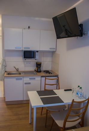 Una cocina compacta con armarios blancos, microondas, cafetera y una pequeña mesa de comedor con sillas.
