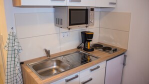 A kitchen with a stainless steel sink, a microwave, a coffee maker, and a refrigerator. - Pension König (Kassel)