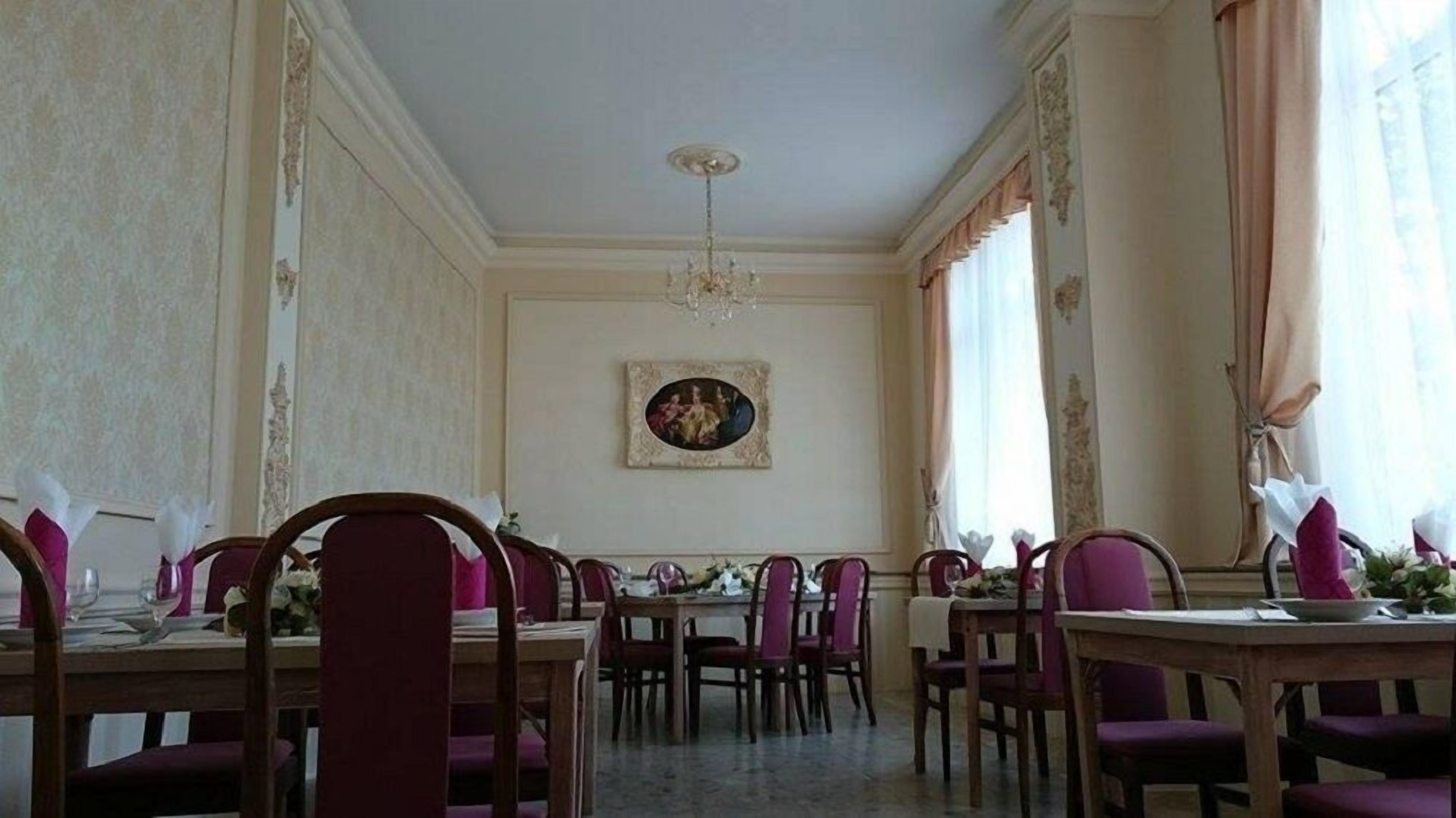 A formal dining room with wooden tables and chairs, a chandelier, and a painting on the wall.