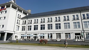Un edificio blanco con múltiples ventanas y balcones, un área de terraza con mobiliario exterior y un cartel que indica un hotel.