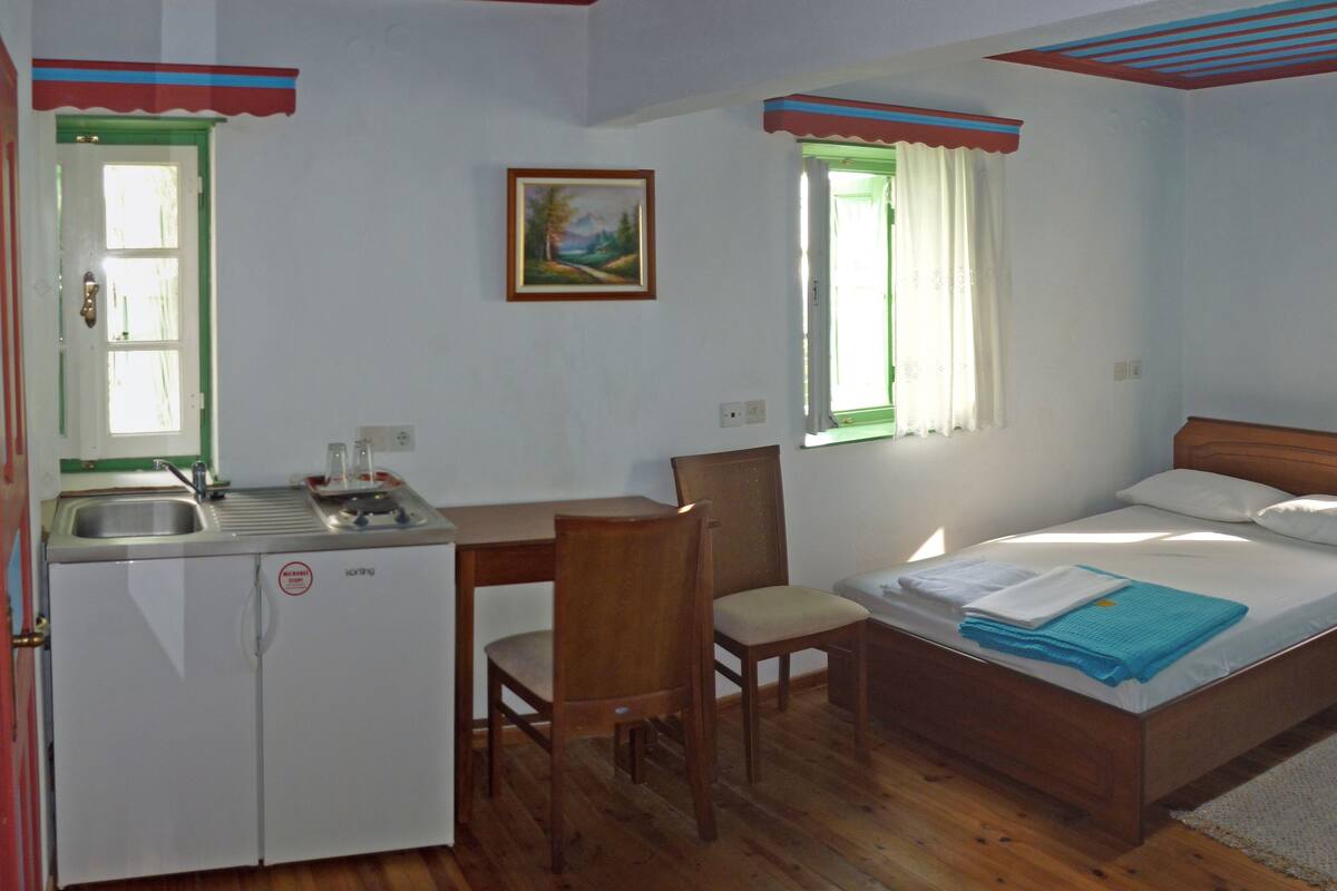 A room with a bed, a desk, a chair, a sink, and a window.