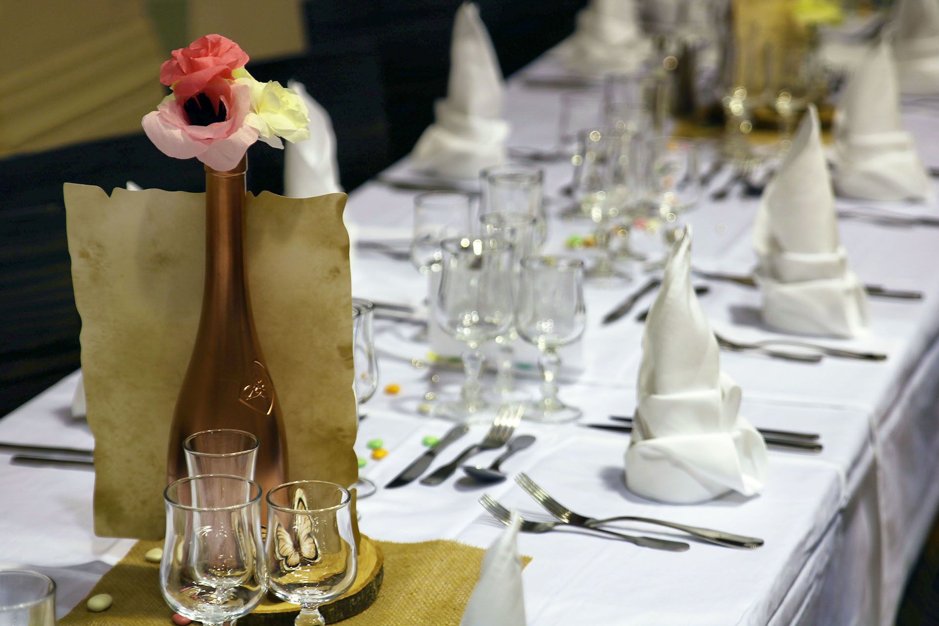 Una mesa dispuesta para un evento formal, con cubertería de cristal, servilletas dobladas y un jarrón decorativo con flores.