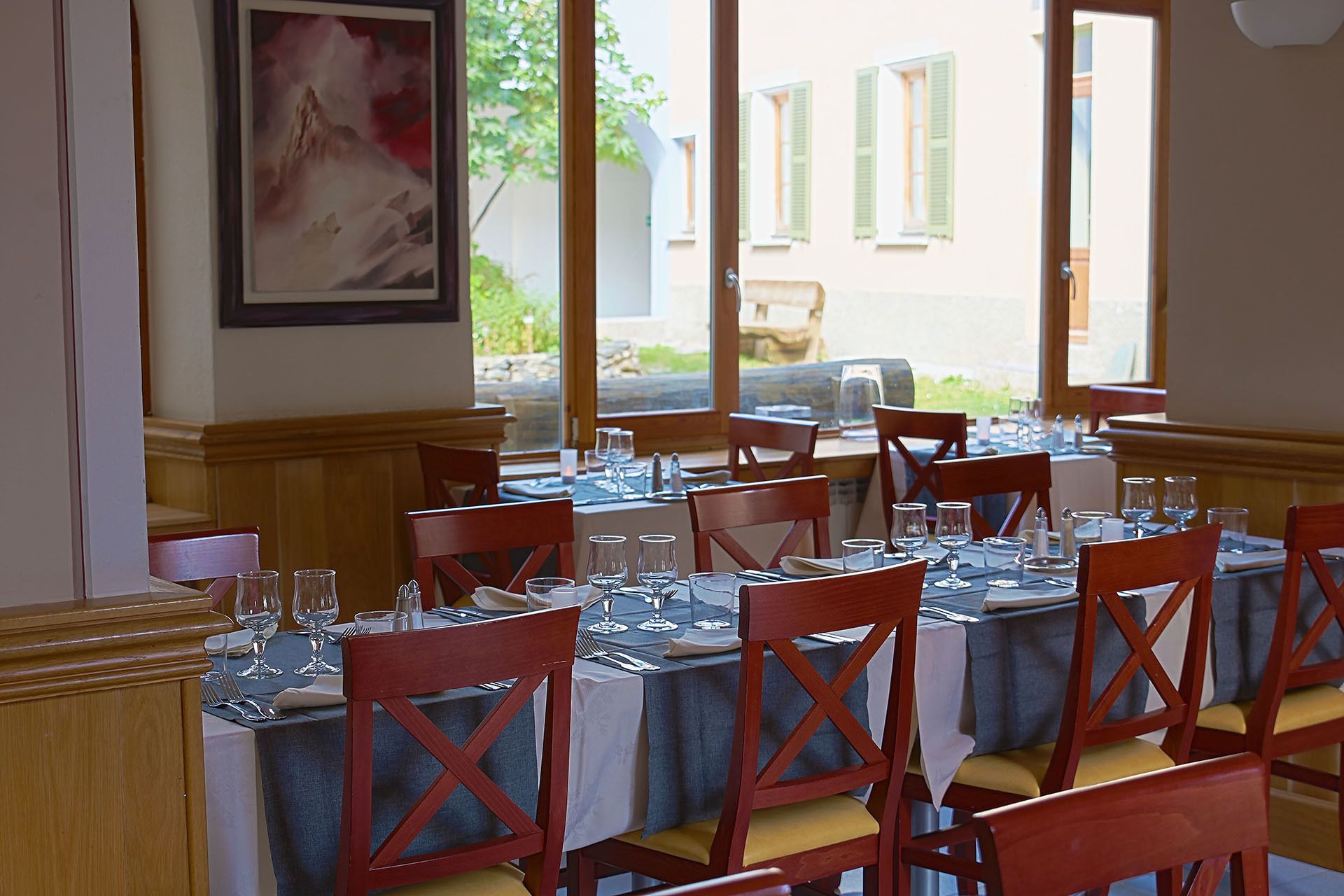 Un espace repas avec des tables dressées pour le repas, des chaises en bois et une vue sur la rue.