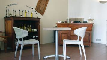 Een zithoek met twee rieten stoelen en een kleine ronde tafel. Op de muur hangt een houten kastje met flessen en een lijst met een foto.