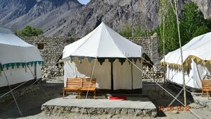 A tented accommodation with a stone wall and a bench in front, set against a mountainous backdrop. - Hunder Sarai (Leh)
