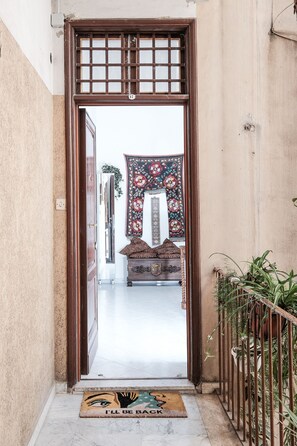 A doorway leading to a room with a patterned tapestry, a wooden chest, and a doormat with a handprint design.
