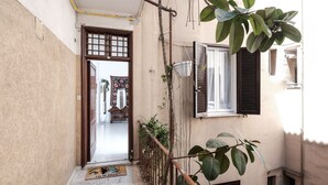 A narrow outdoor corridor with a wooden door leading to a room with a patterned rug. - Domus Linda (Rome)