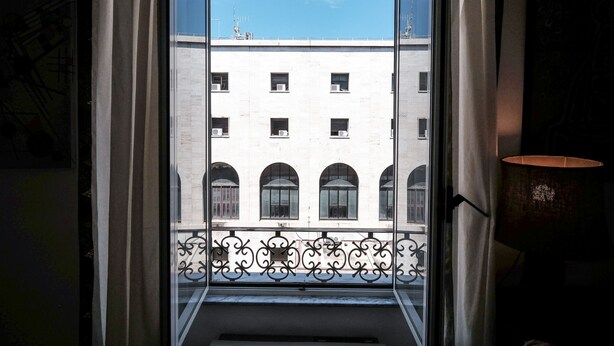 A view from a window with a balcony, featuring a building with multiple windows and balconies, and a clear blue sky. - Domus Linda (Rome)