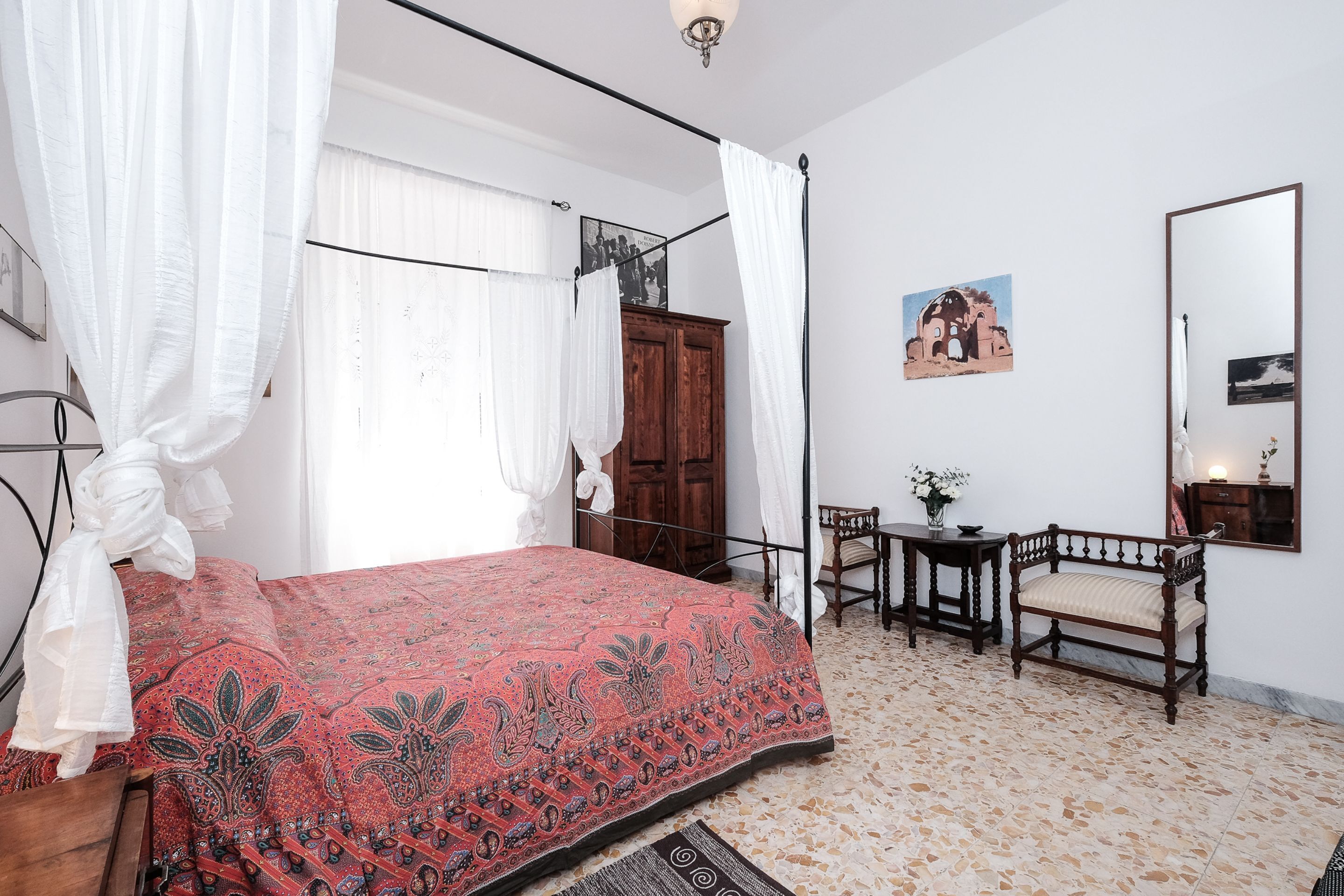 Une chambre à coucher avec un lit à baldaquin, une armoire en bois, une petite table avec une chaise et un miroir au mur.