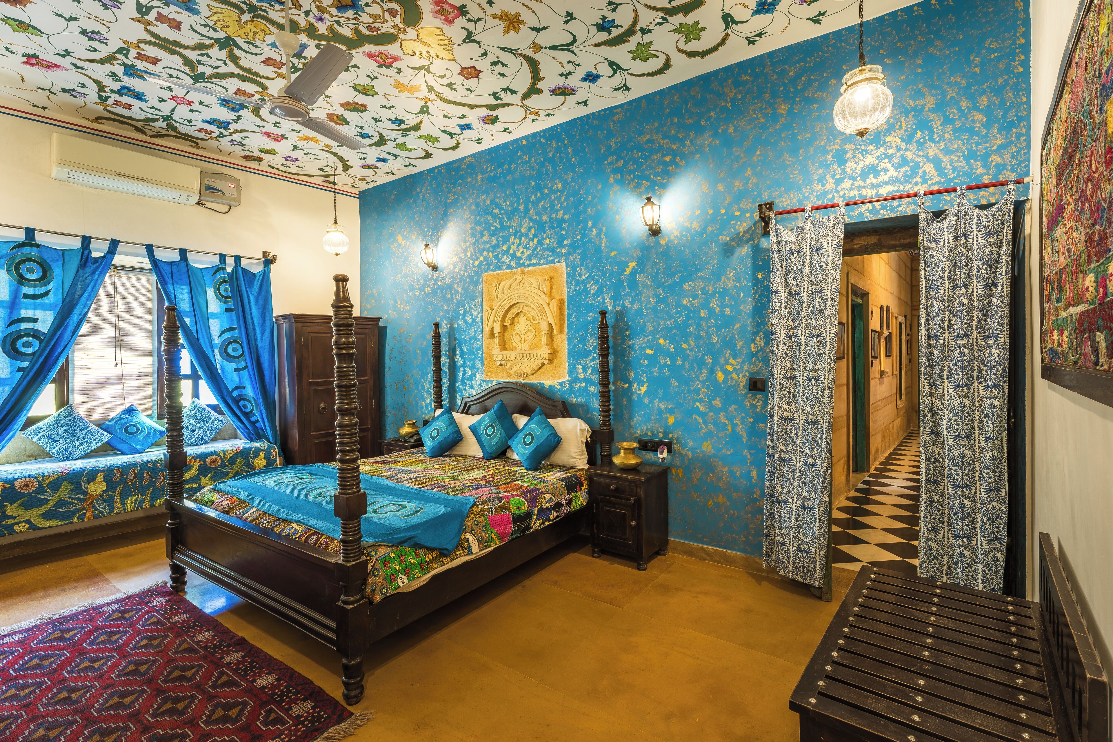 Ein Schlafzimmer mit Himmelbett, einem gemusterten Teppich und einer blauen und goldenen Wandgestaltung.