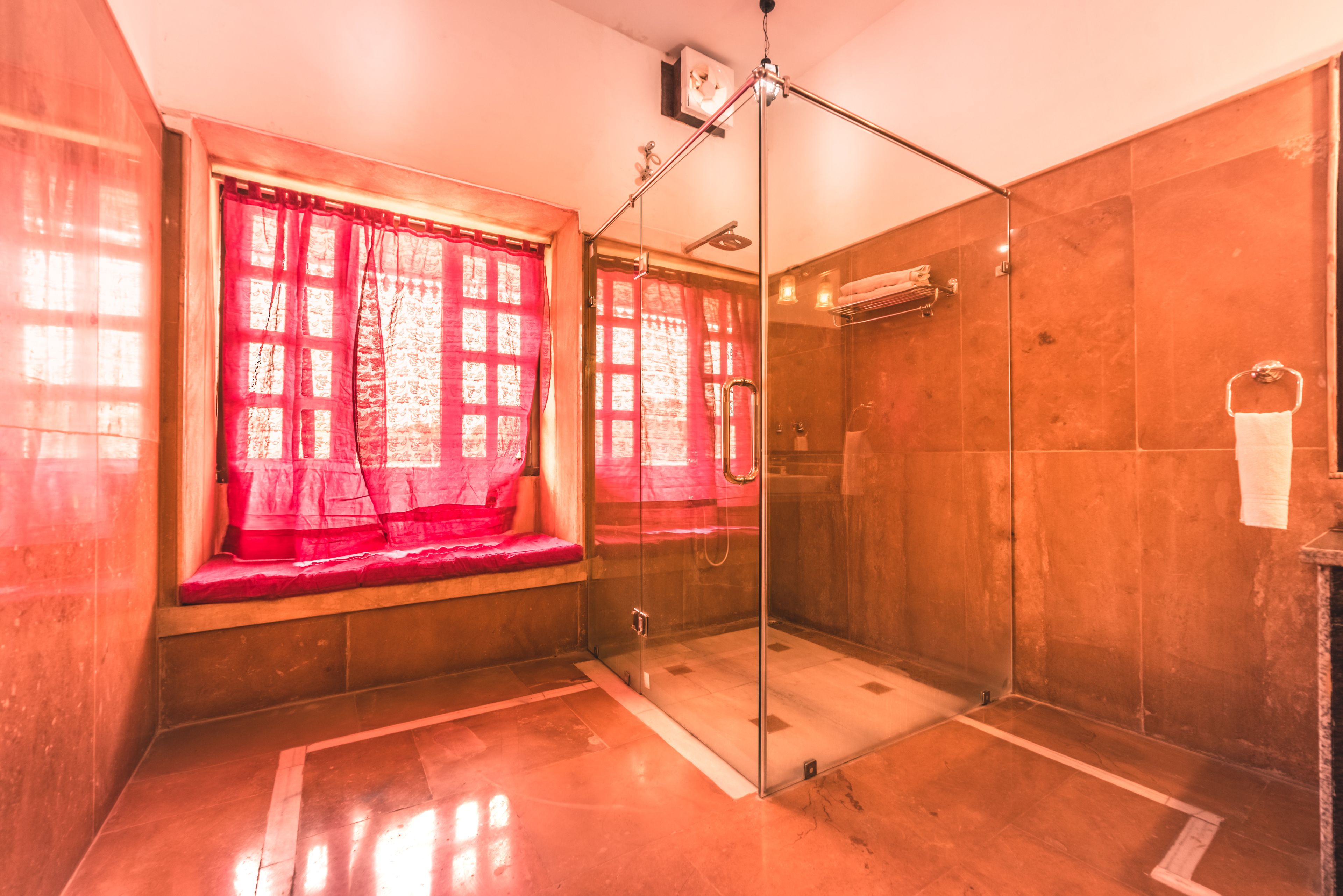 A modern bathroom with a glass shower enclosure, a bench by the window, and a towel rack.