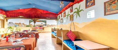 Un comedor con mesas preparadas para dos, bancos y un mural de palmeras en la pared.