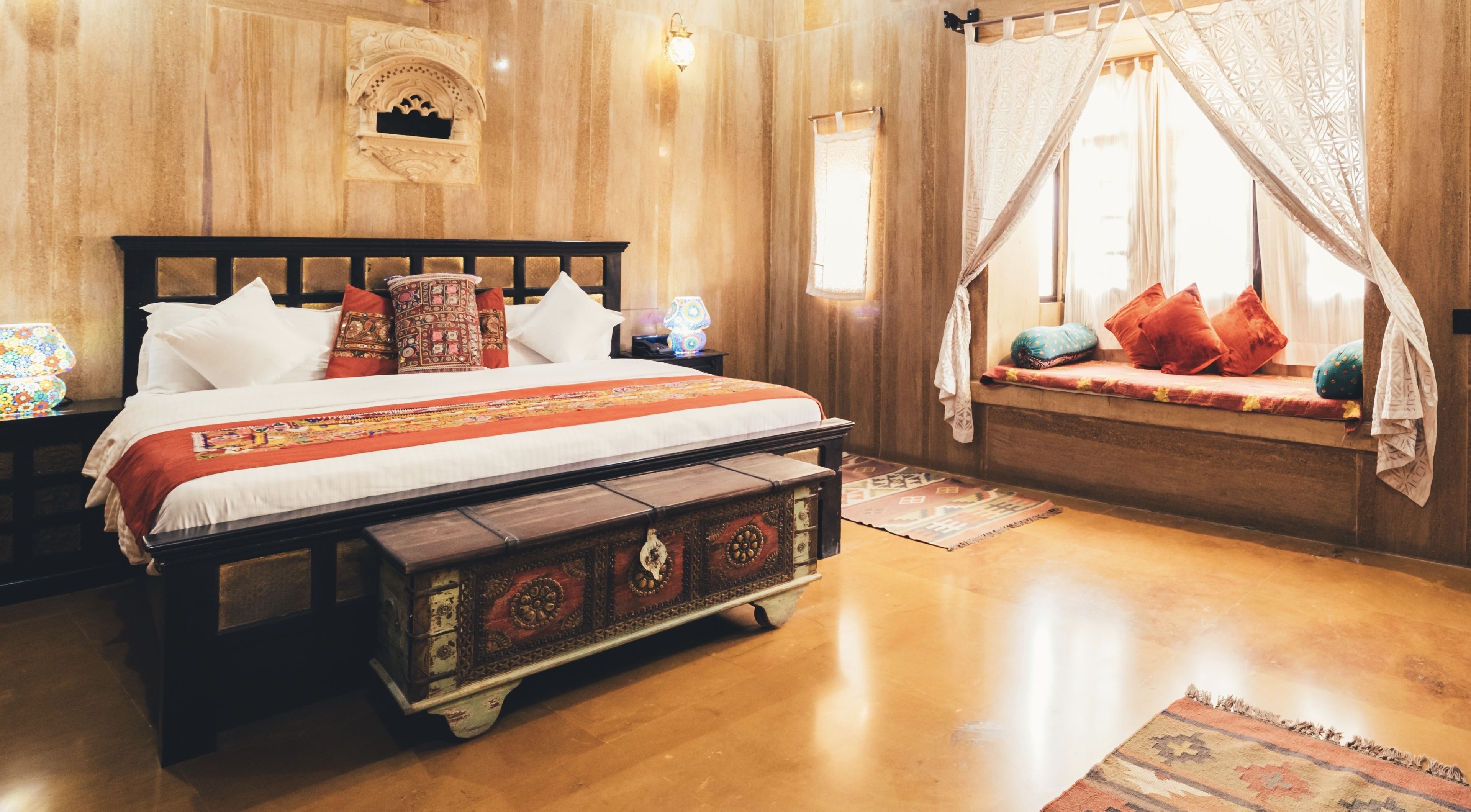A traditional wooden bed with a canopy, a nightstand with a lamp, and a window seat with cushions.
