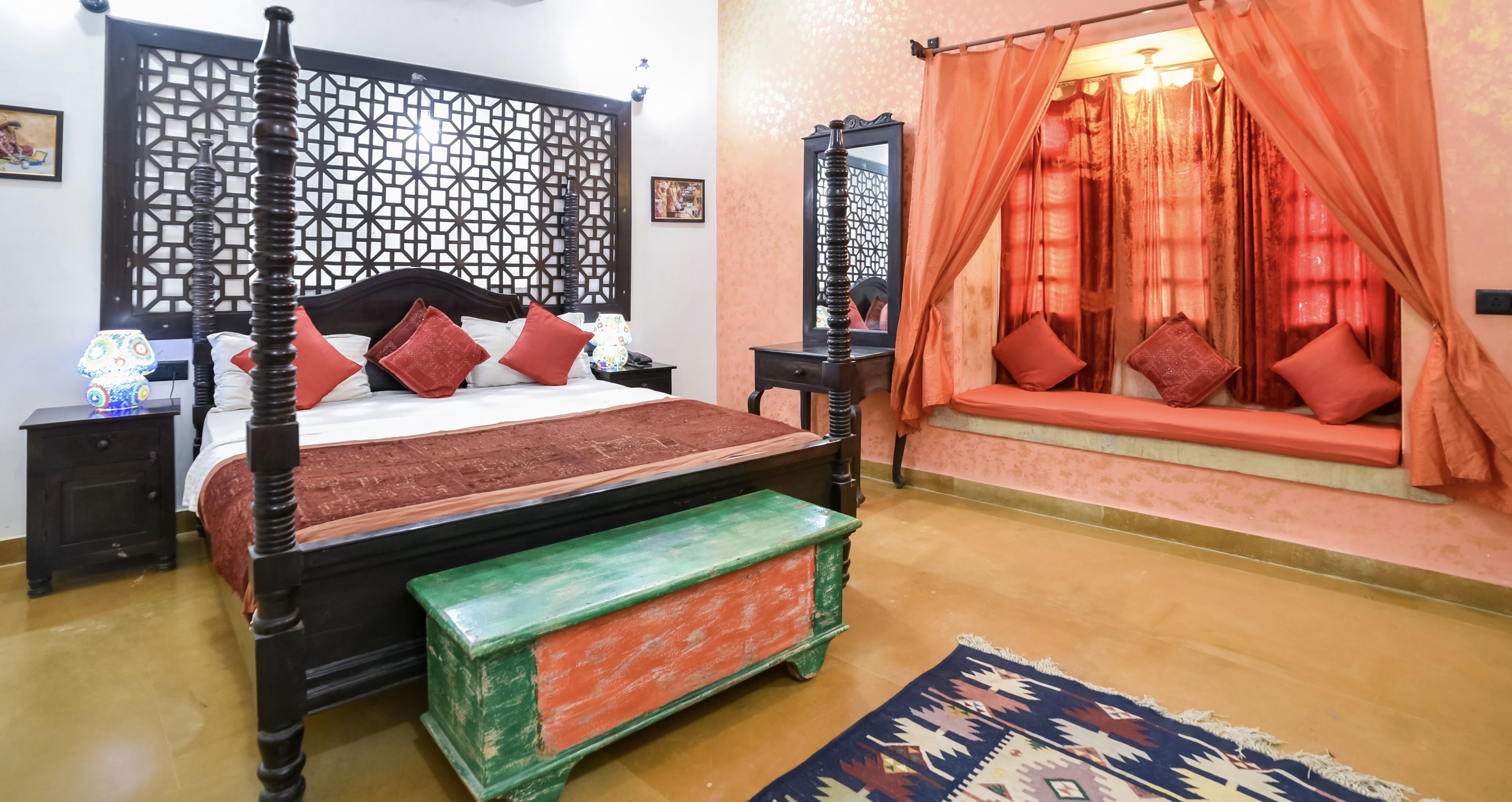 A four-poster bed with red and white bedding, a green bench, and a patterned rug.