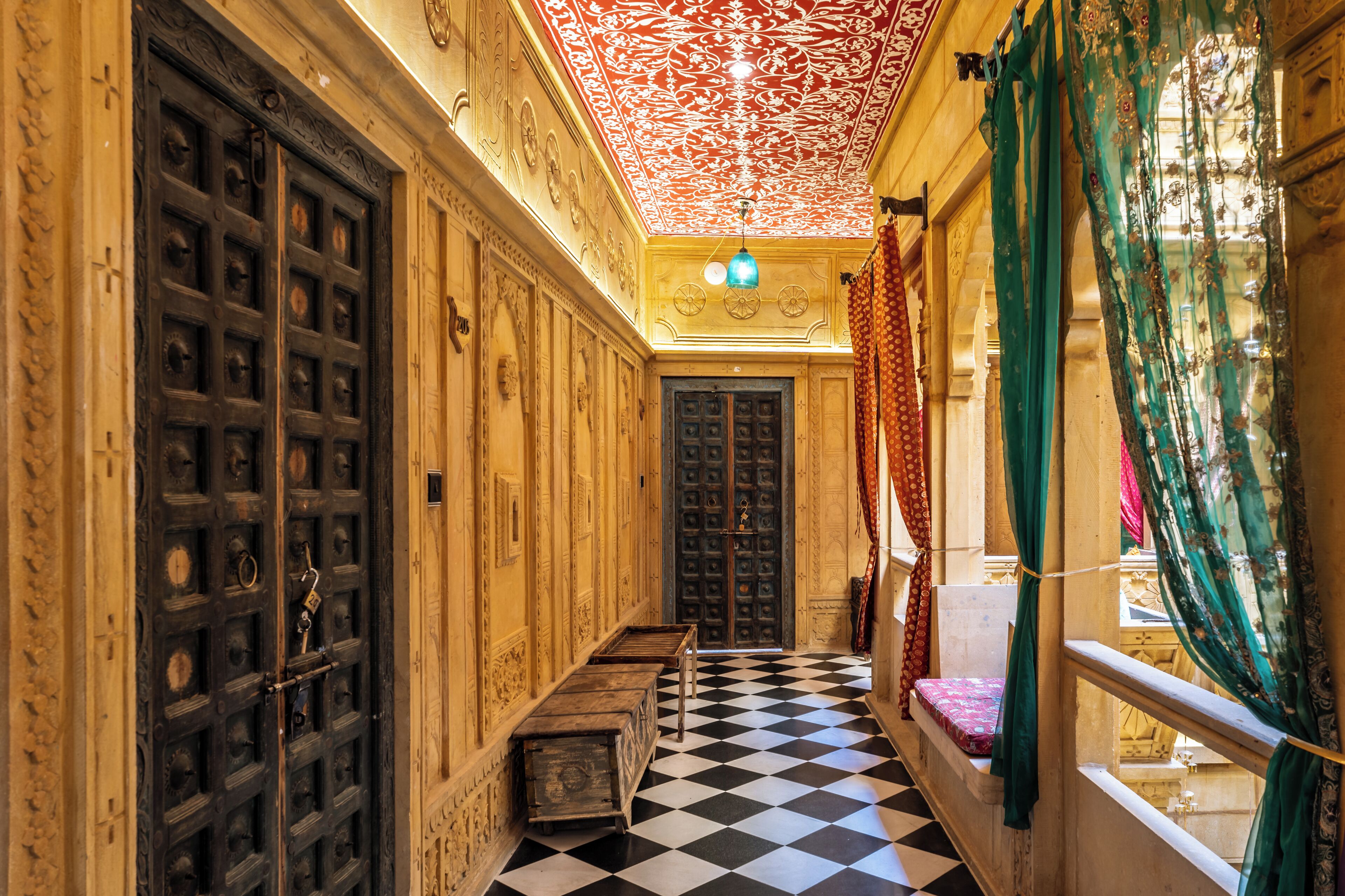 A corridor with ornate doors, a checkered floor, and a view through a window with green curtains.